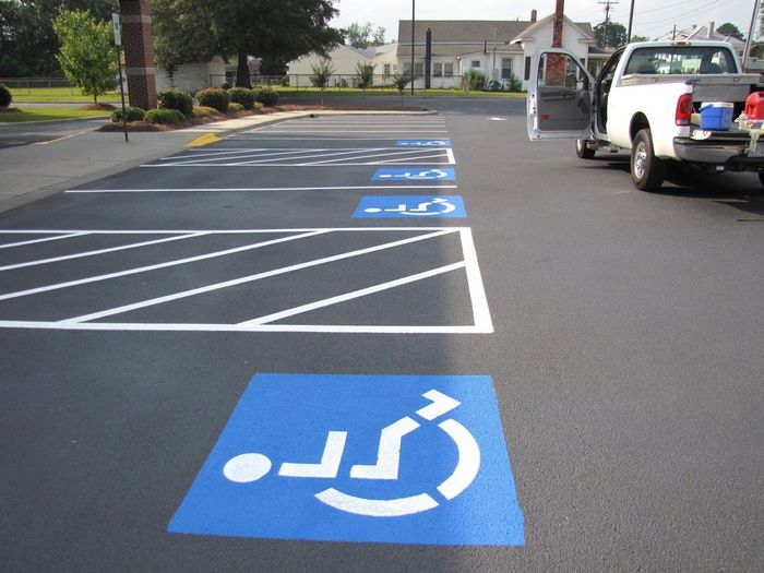 Freshly painted blue and white accessible parking spaces in a parking lot, with a pickup truck parked nearby.