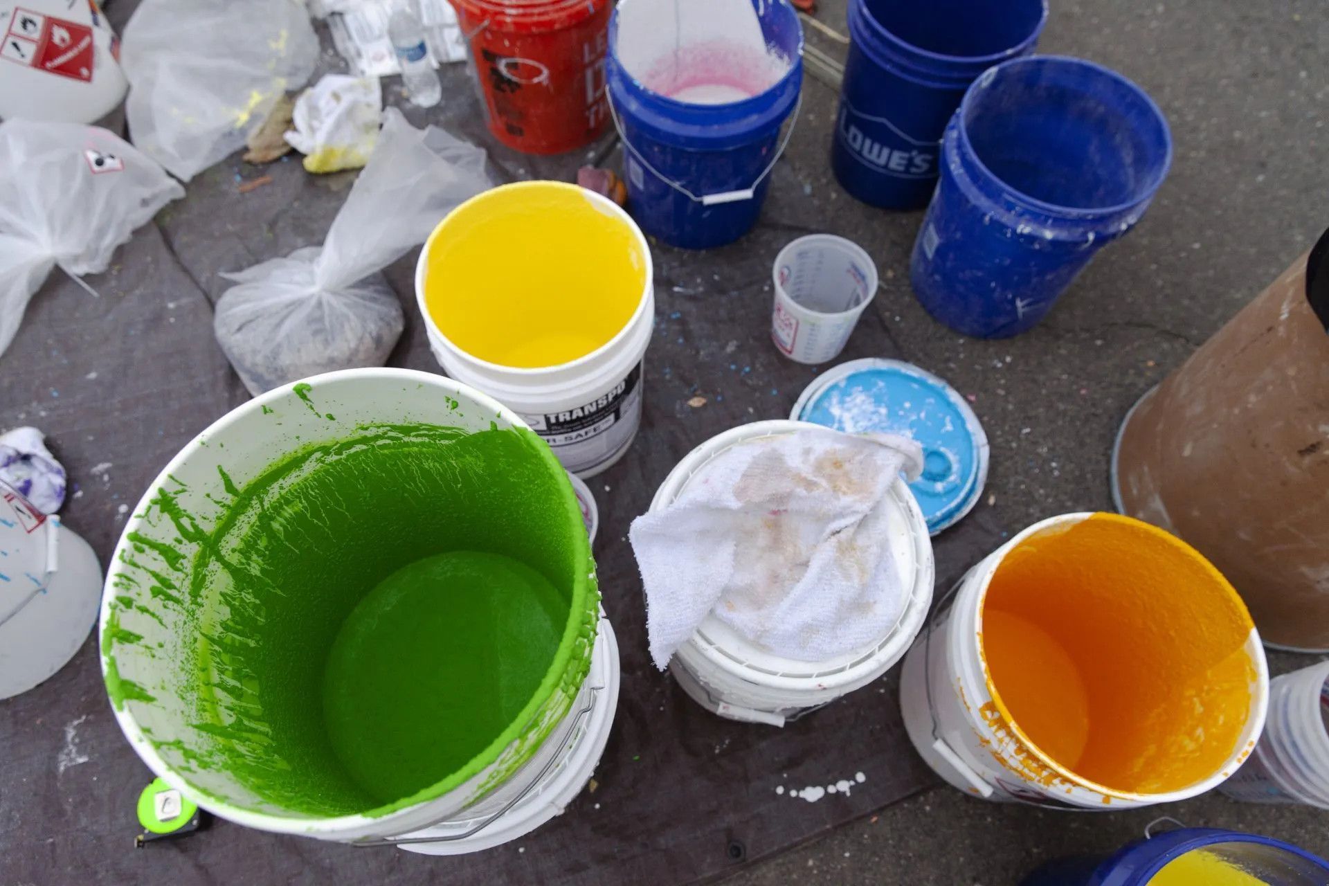 An array of paint buckets filled with vibrant colors—green, yellow, and orange—sitting on a ground cloth.