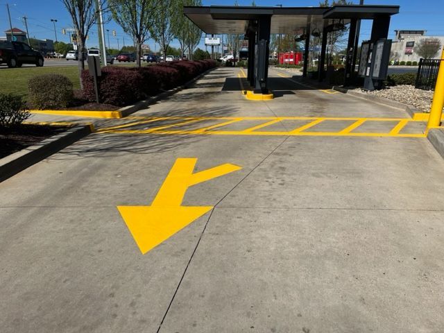 Yellow directional arrow painted on pavement leading to a gated entrance curbside pickup lane.