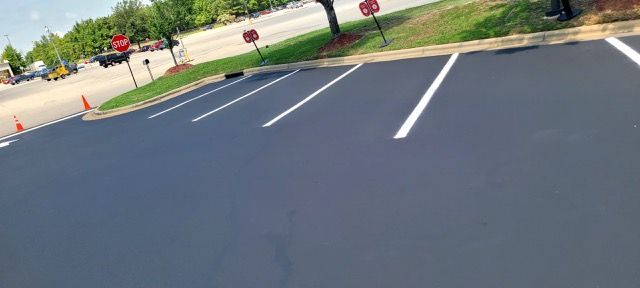 Empty parking lot with fresh white lines and orange cones along the edge near a grassy sidewalk.