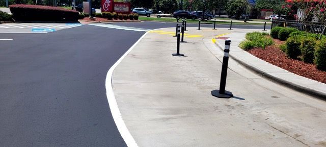 Curved sidewalk with black bollards beside a paved road and landscaped shrubs in bright daylight