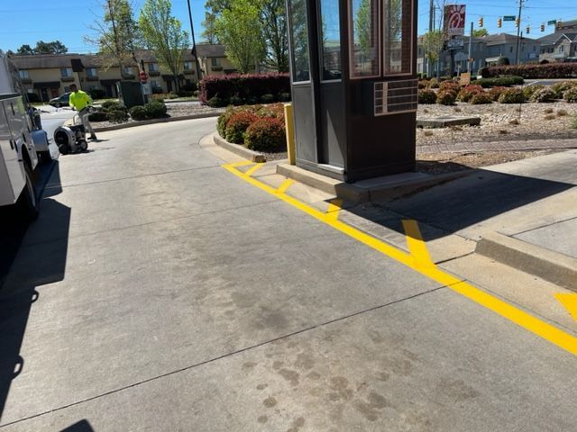 Drive-through lane with a curbside kiosk, yellow markings, and parked cars on a sunny day