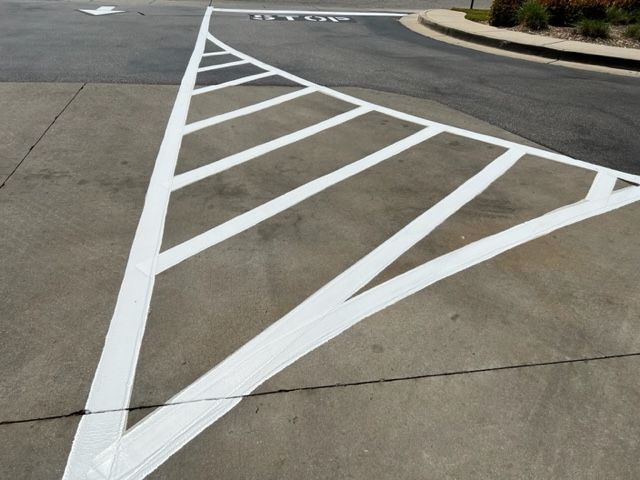 White painted diagonal road markings on a concrete intersection with a curved curb.