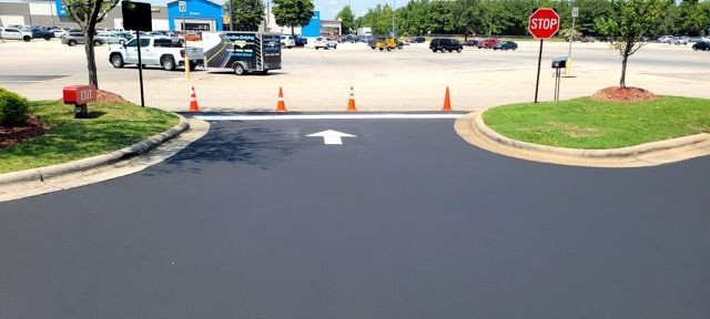 Parking lot entrance blocked by cones and barricade, with stop sign and white directional arrow on pavement