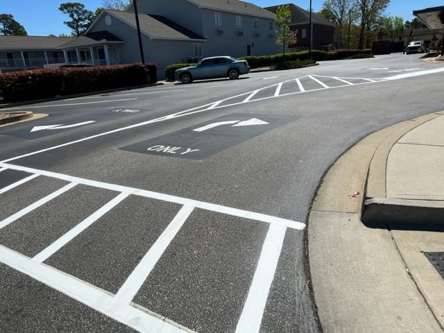 Street intersection with white lane markings, a crosswalk ramp, and a car passing by houses on a sunny day