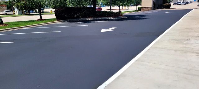 Empty parking lot with freshly paved dark asphalt and a concrete sidewalk on the right