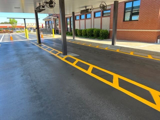 Covered drive-through lane with yellow painted curb markings beside a brick building