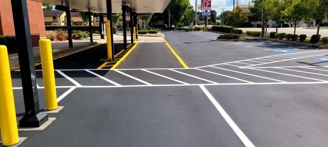 Parking lot with white crosswalk lines, yellow curbs, and yellow bollards near a storefront.