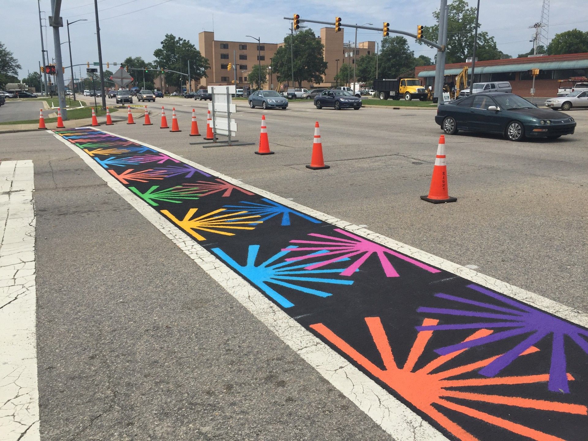 Colorful temporary curb lane mural with orange cones blocking a city street intersection