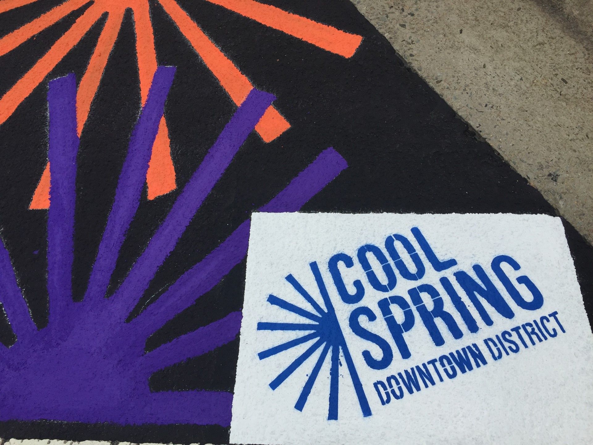 Cool Spring Downtown District sign with blue text on white, beside purple and orange abstract design