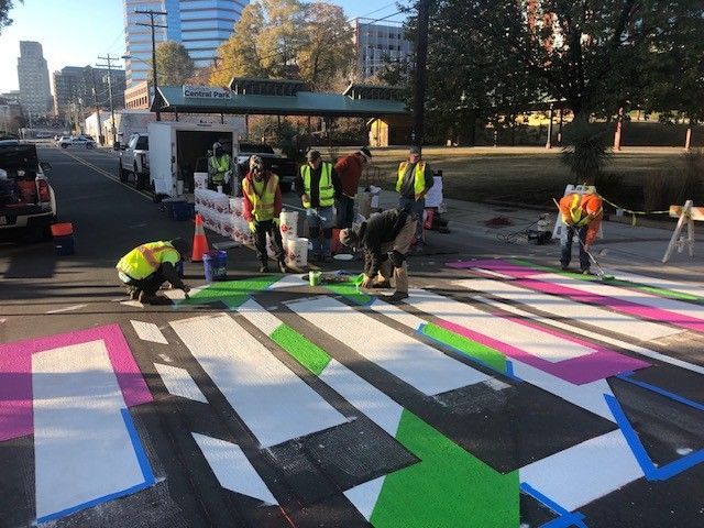 Workers painting colorful geometric street mural on a roadway in daylight