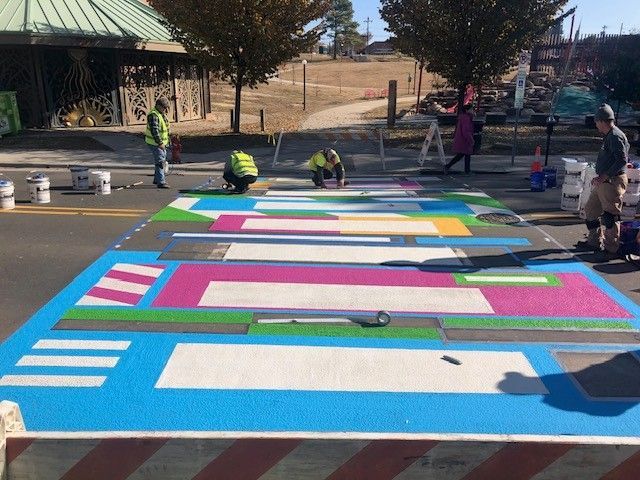 People painting a large colorful pavement mural outdoors on a sunny day.