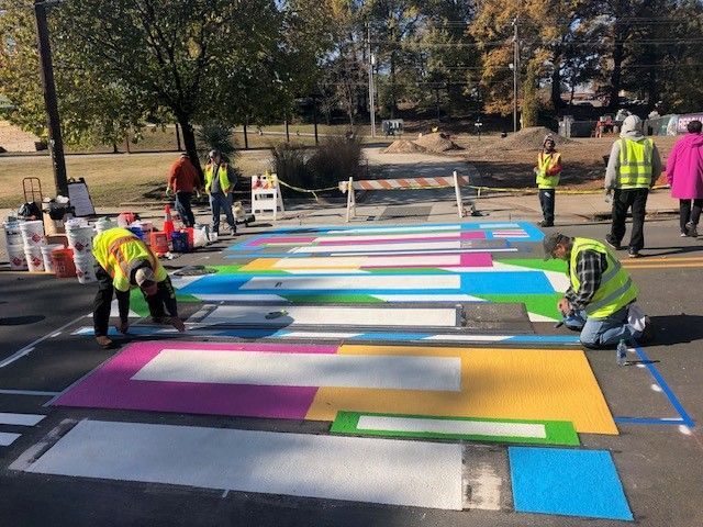 Workers painting a colorful giant puzzle on pavement outdoors