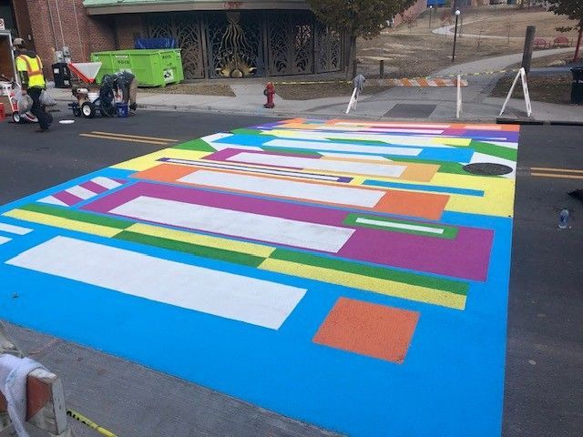 Colorful geometric street mural being painted on asphalt near a road crew and cones
