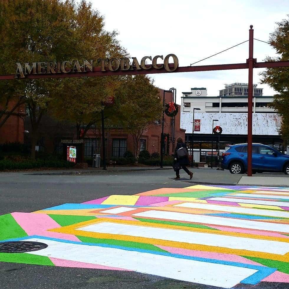 Colorful geometric street mural in the foreground with American Tobacco buildings and a pedestrian crossing nearby