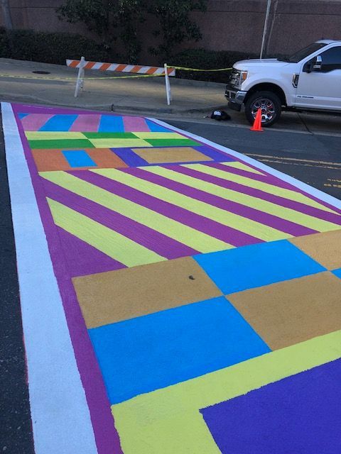 Colorful striped street mural on a road, with a white pickup truck parked beside it and traffic cones nearby