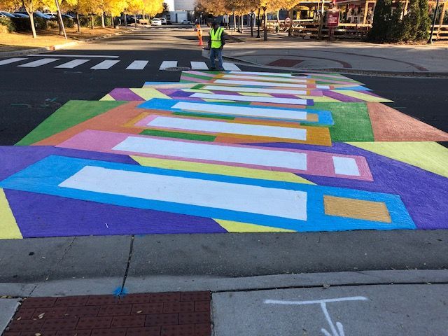 Colorful painted crosswalk with geometric stripes on a street at an intersection.