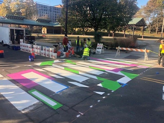 Workers painting colorful geometric street art on an intersection in daylight