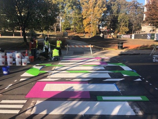 Colorful road crosswalk being painted with workers on a street in a park area