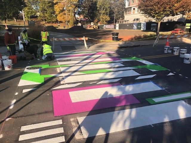 Workers painting colorful crosswalk stripes on a street at a construction site
