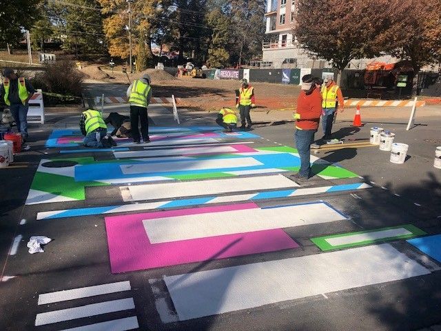 Workers painting colorful rectangular pavement markings in a parking lot