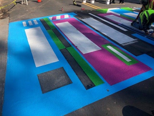 Colorful painted parking lot with blue, pink, green, and white rectangles, plus a worker at the right edge