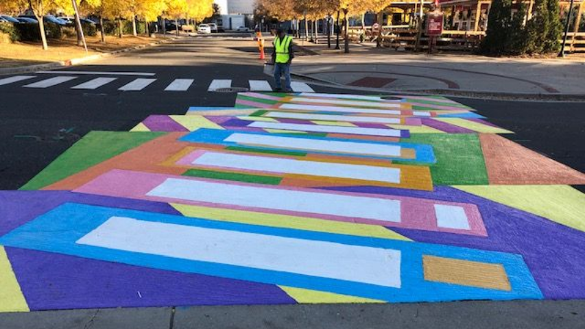 Colorful painted crosswalk with geometric patterns on a street, with a worker in a safety vest in the background in Durham, NC