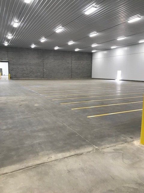 Empty indoor warehouse with concrete floor, white walls, and overhead lights