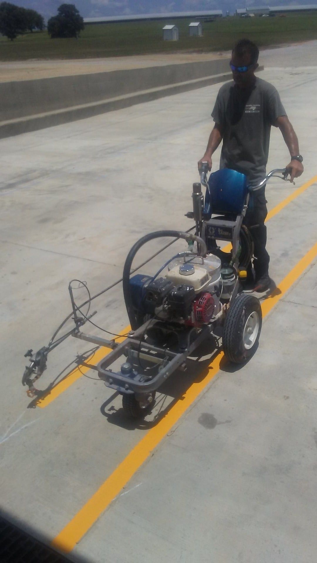 Person pushing a small wheeled engine machine on a concrete runway or road.