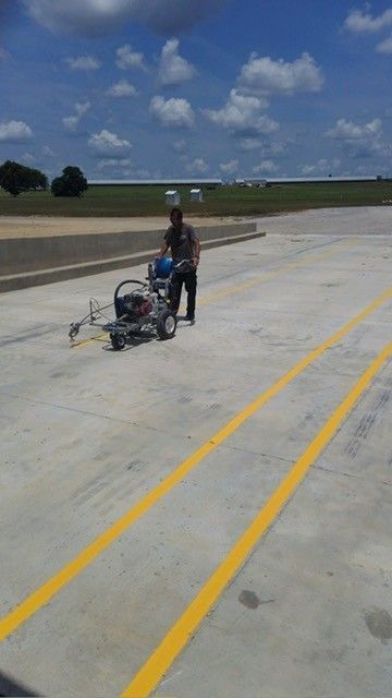 Person pushing a stroller on a sunlit concrete roadway with yellow lines under a blue sky