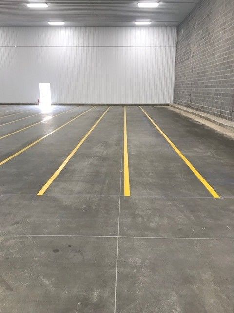 Empty indoor warehouse space with concrete floor, yellow parking lines, and white metal walls