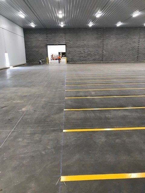 Empty warehouse interior with gray concrete floor, yellow lane markings, and overhead lights