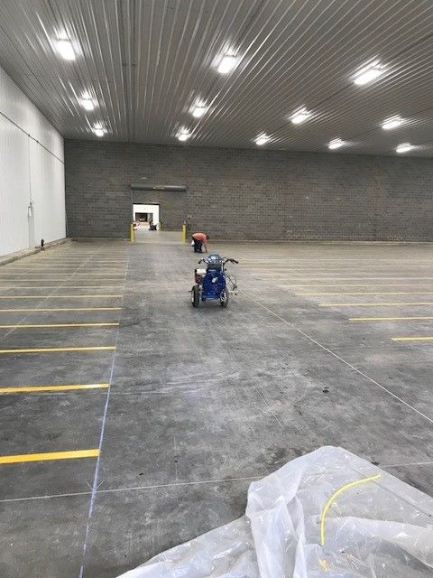 Large empty warehouse with concrete floor, ceiling lights, and two wheelchairs near the center.