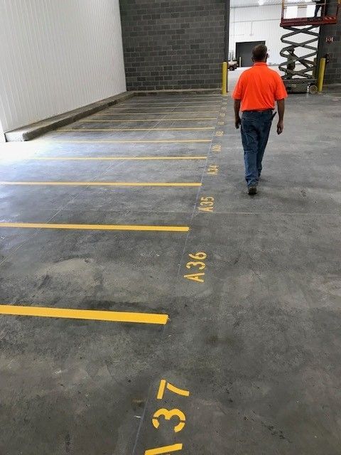 Man in orange shirt walking through marked parking spaces in a concrete garage