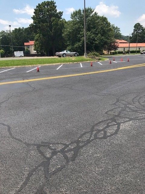 Parking lot with cones cordoning off a section of cracked asphalt near trees and a building