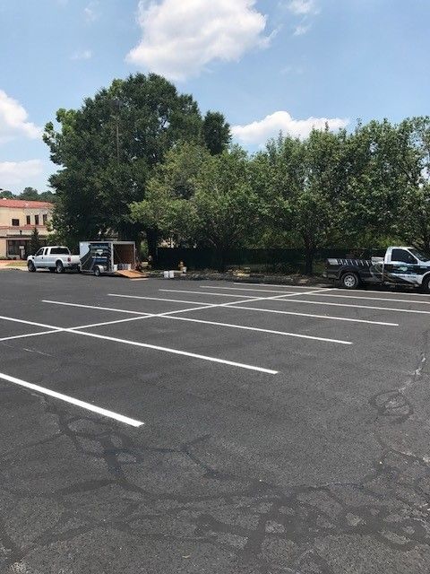 Empty parking lot with white lines, trees, and parked vehicles under a partly cloudy sky
