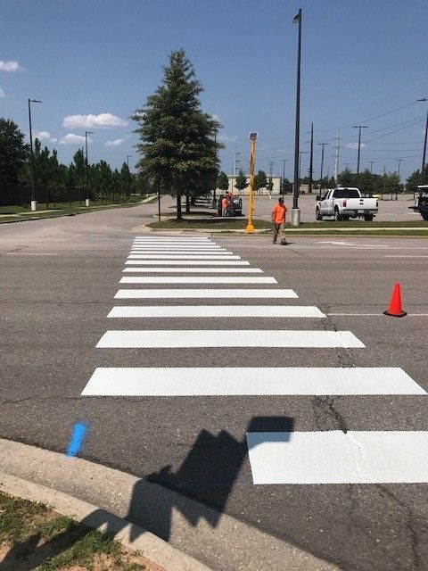Pedestrian crosswalk with white stripes and orange cones on an empty roadway under a sunny sky