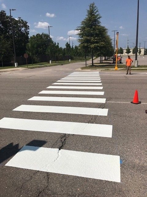 Marked crosswalk on a road with orange cones and workers in the distance, sunny day