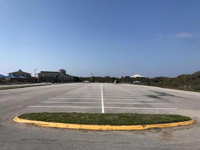 Empty parking lot with white lines and a yellow curb under a clear blue sky.