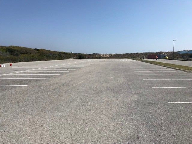 Empty paved parking lot under a clear sky, with trees lining the edges