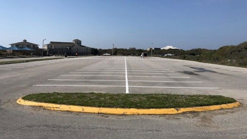Empty parking lot with white lines and a yellow curb under a clear blue sky in Port Fisher, NC