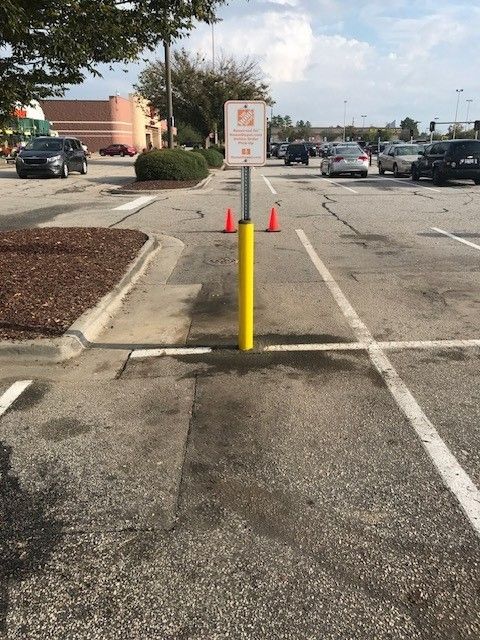 Parking lot with yellow bollard, orange cones, and a sign marking a pedestrian access area