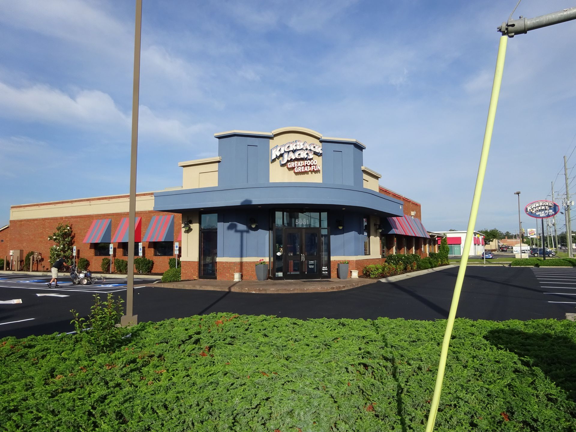 Restaurant storefront with blue awning, glass entrance, and parking lot under a sunny sky