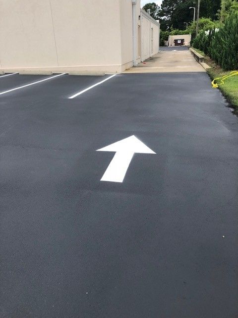 Freshly paved parking lot with a white directional arrow pointing forward beside a beige building