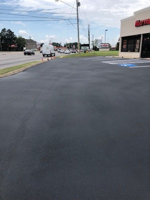 Parking lot beside a storefront with fresh black asphalt and a road in the background
