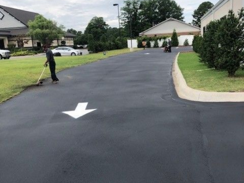 Worker painting a white arrow on a dark asphalt driveway in a suburban neighborhood in Raleigh, NC