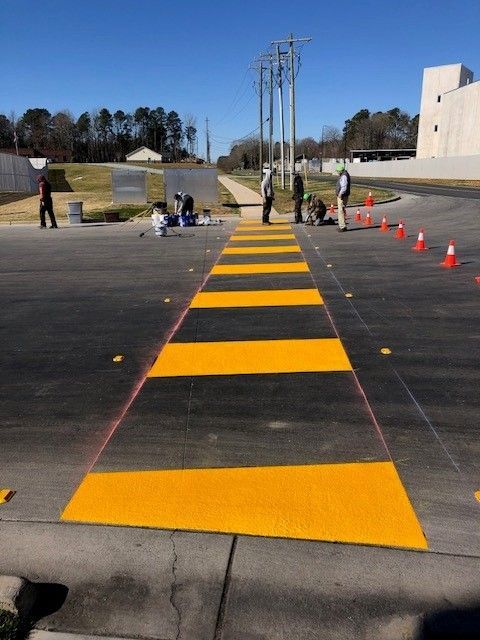 Yellow-and-black striped test path on pavement with people and orange cones in an outdoor lot