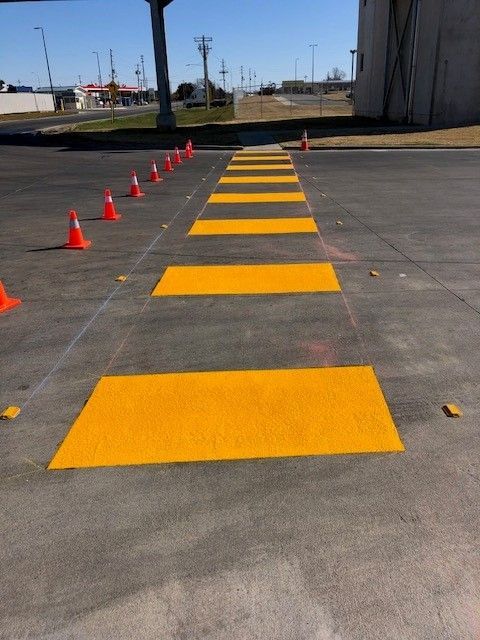 Orange cones lining a yellow painted path on dark pavement outdoors, near a building and open road