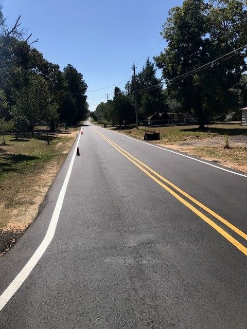 Empty two-lane road with yellow center lines through a tree-lined park on a sunny day