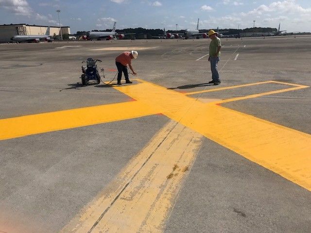 Workers painting a bright yellow X on an airport tarmac
